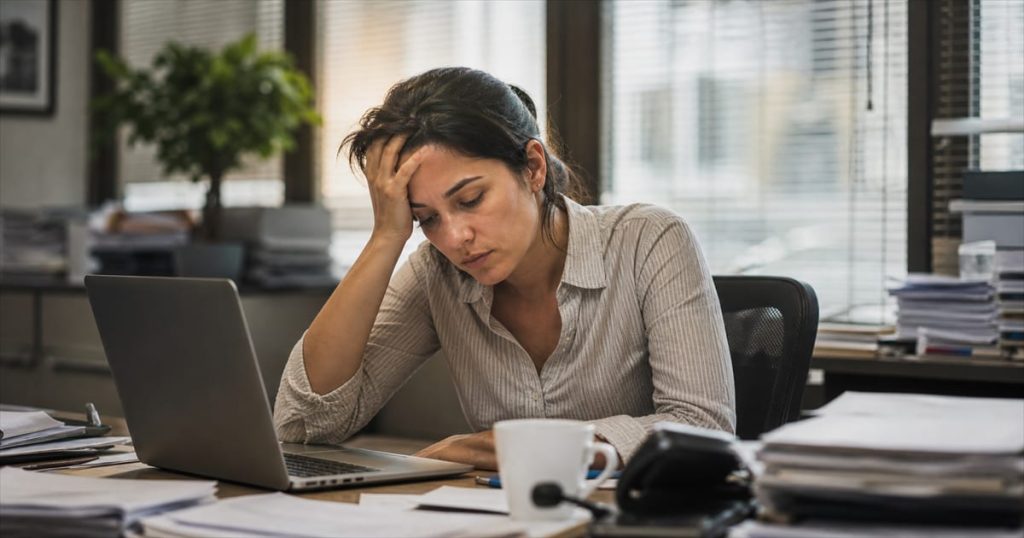 Profissional brasileira exausta em mesa de trabalho com sinais de burnout