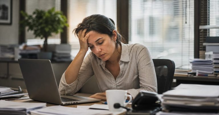 Profissional brasileira exausta em mesa de trabalho com sinais de burnout